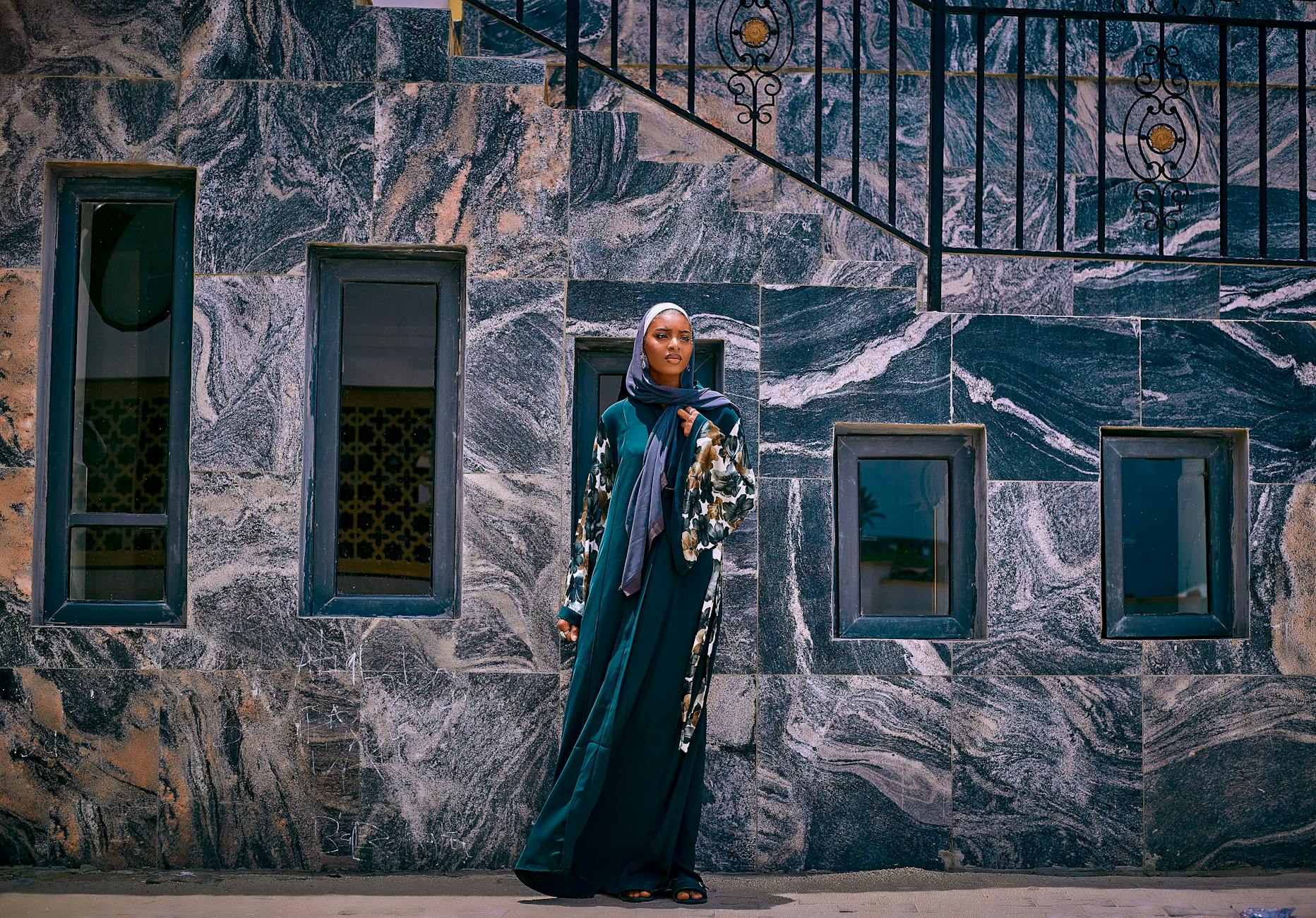 Woman stands gracefully by marble wall in traditional dress, exuding elegance.