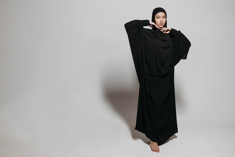 Portrait of a woman in a stylish black abaya striking a pose on a neutral background.